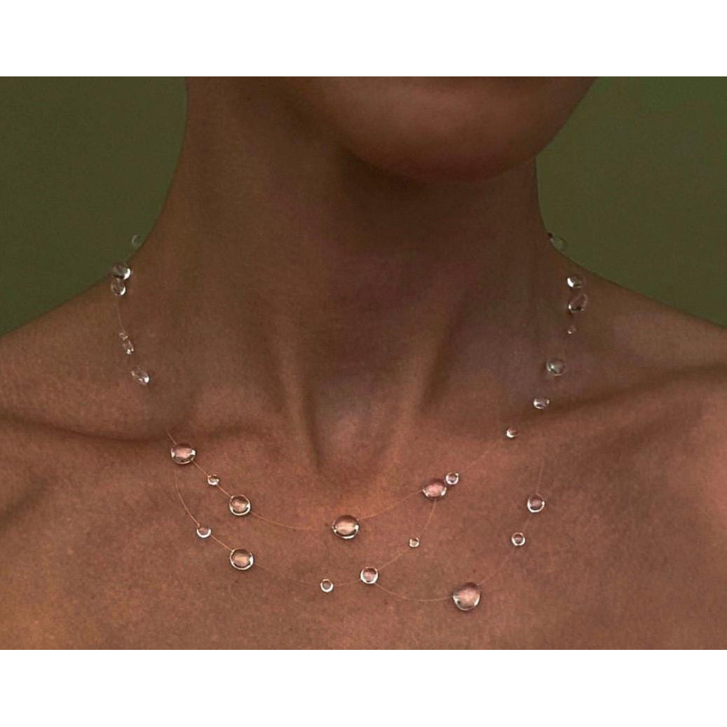 Necklace with small, round, clear beads on a person's neck against a green background