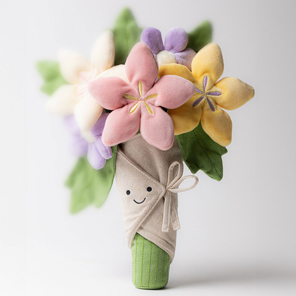 A plush toy bouquet featuring a smiling beige wrapped stem, green leaves, and three fabric flowers in cream, pink, and lavender, set against a plain white background.
