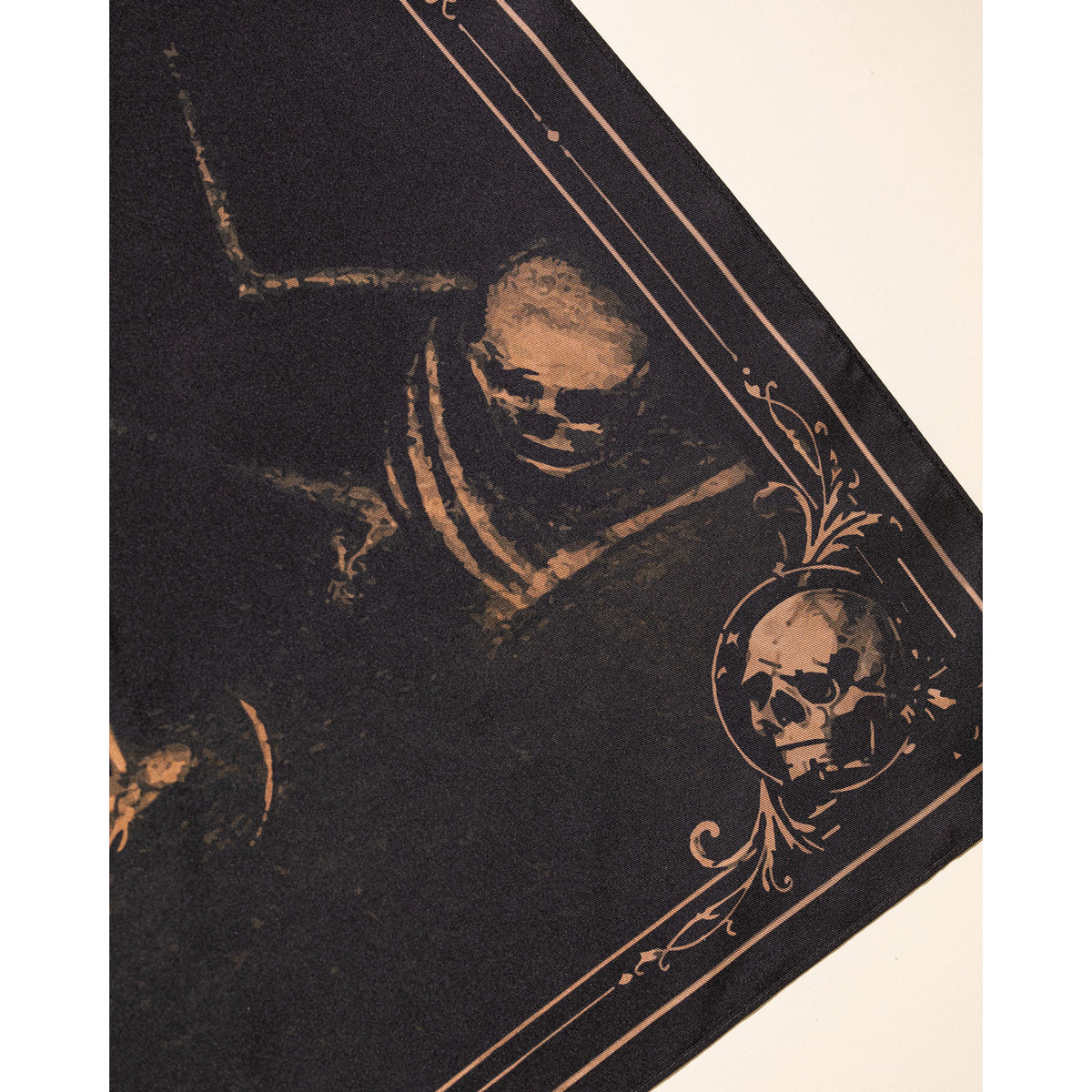 A close-up of a dark gothic textile or print featuring a skull illustration and ornate beige decorative border on a cream background.