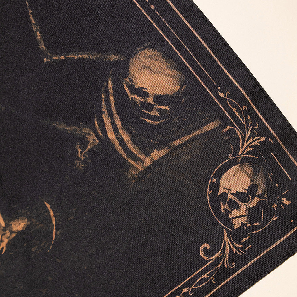 A close-up of a dark gothic art print featuring a skull in a circular frame with ornate scrollwork, printed in a sepia-toned ink on a black background.