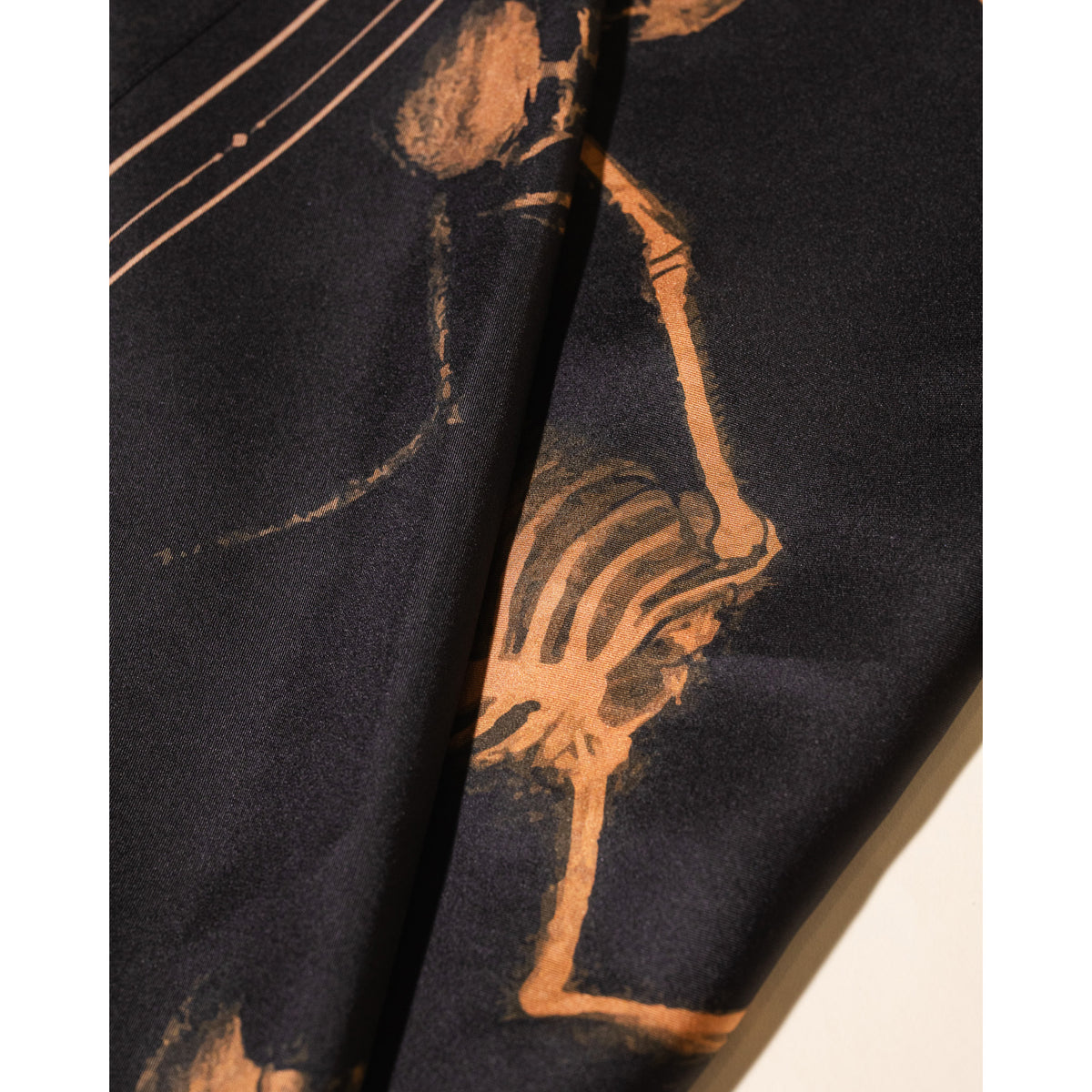 A close-up of a black fabric with a stylized tan skeleton print, draped to show its texture and pattern.