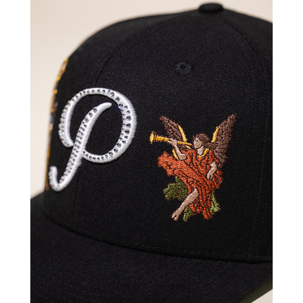 Black cap with embroidered design of an angel playing a trumpet and a large letter 'P'.