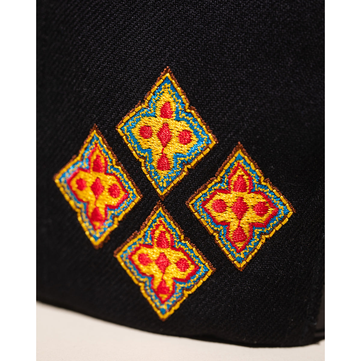 Black fabric with four embroidered red and yellow geometric patterns