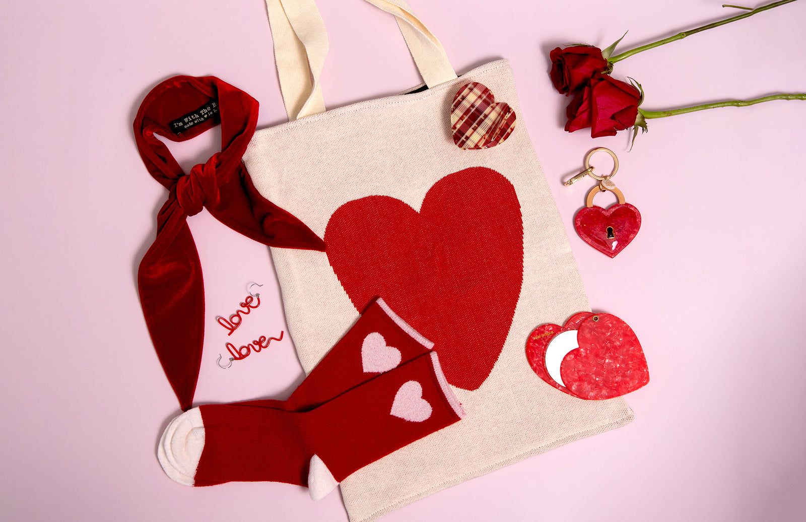 Tote bag with heart designs, socks, and keychain on a pink background