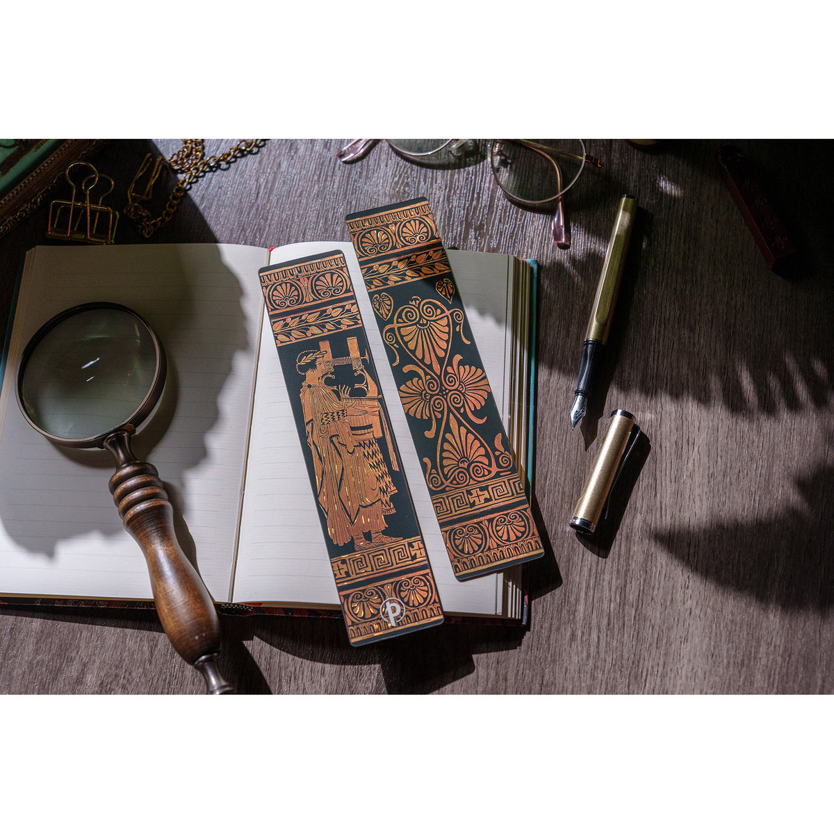 Decorative bookmarks with intricate designs on a wooden surface with a magnifying glass and pen.