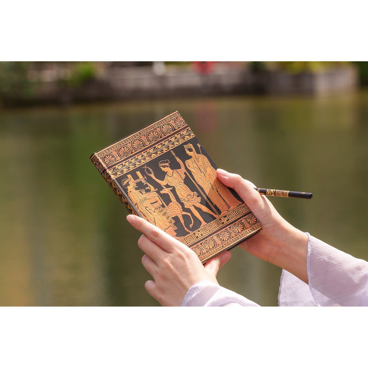 Decorative notebook with artistic cover held by hands against a blurred natural background