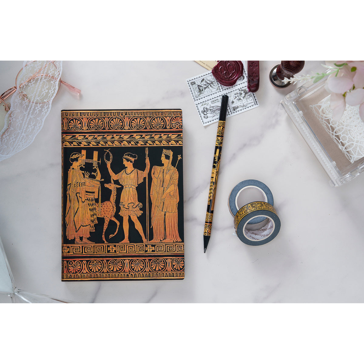 Decorative notebook with classical design on a white surface with stationery items.
