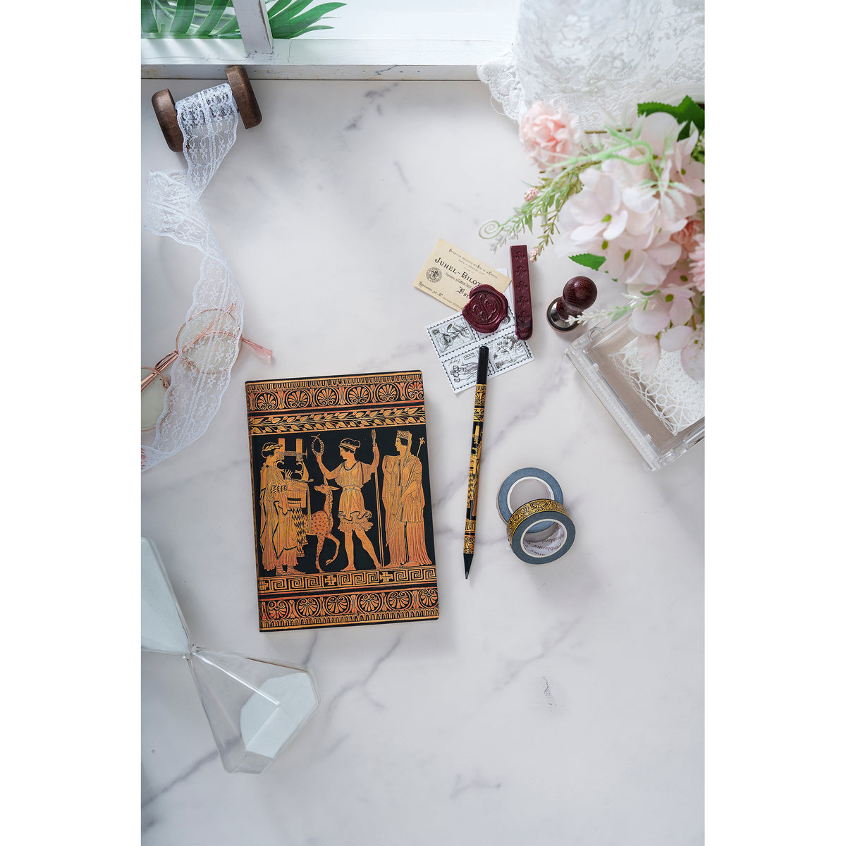 Decorative notebook with classical design on a marble surface with stationery items.
