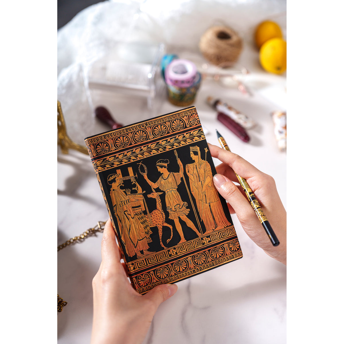 Hand holding a decorative notebook with intricate designs on a light background