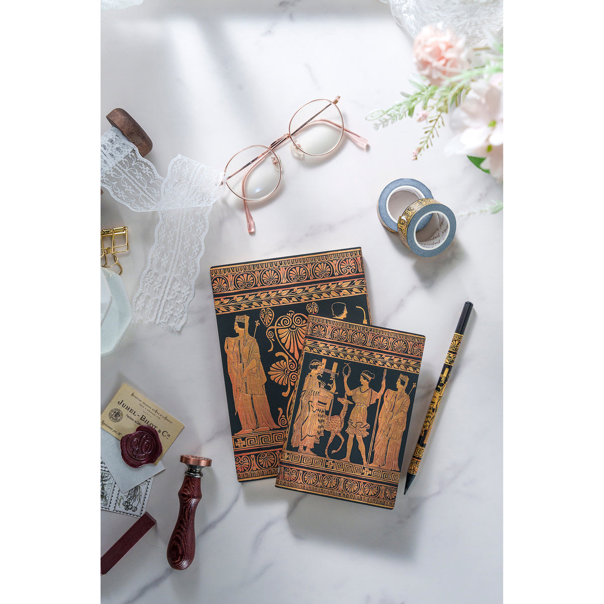 Two ornate notebooks on a white surface with stationery items around