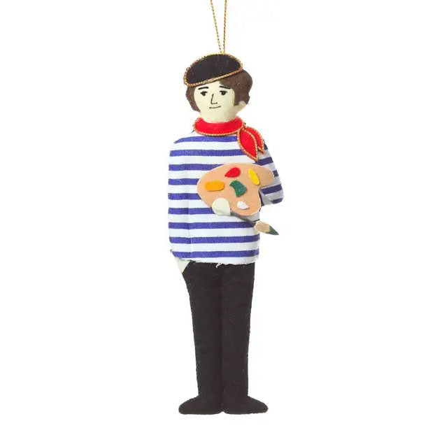 A felt artist hanging ornament shaped like a man wearing a blue and white striped shirt, black pants, a brown beret, and holding a paint palette with colorful paint splotches, on a white background.