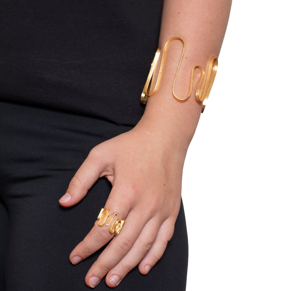 Gold bracelet and ring on a person's wrist and hand against a black background