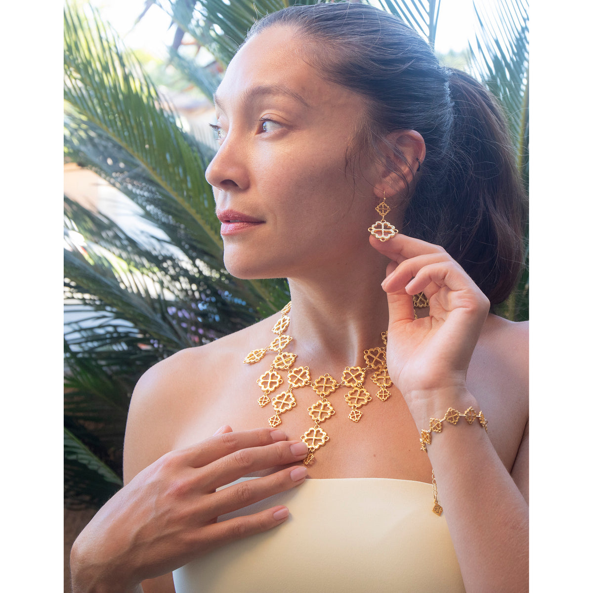 Woman wearing gold jewelry with a tropical background