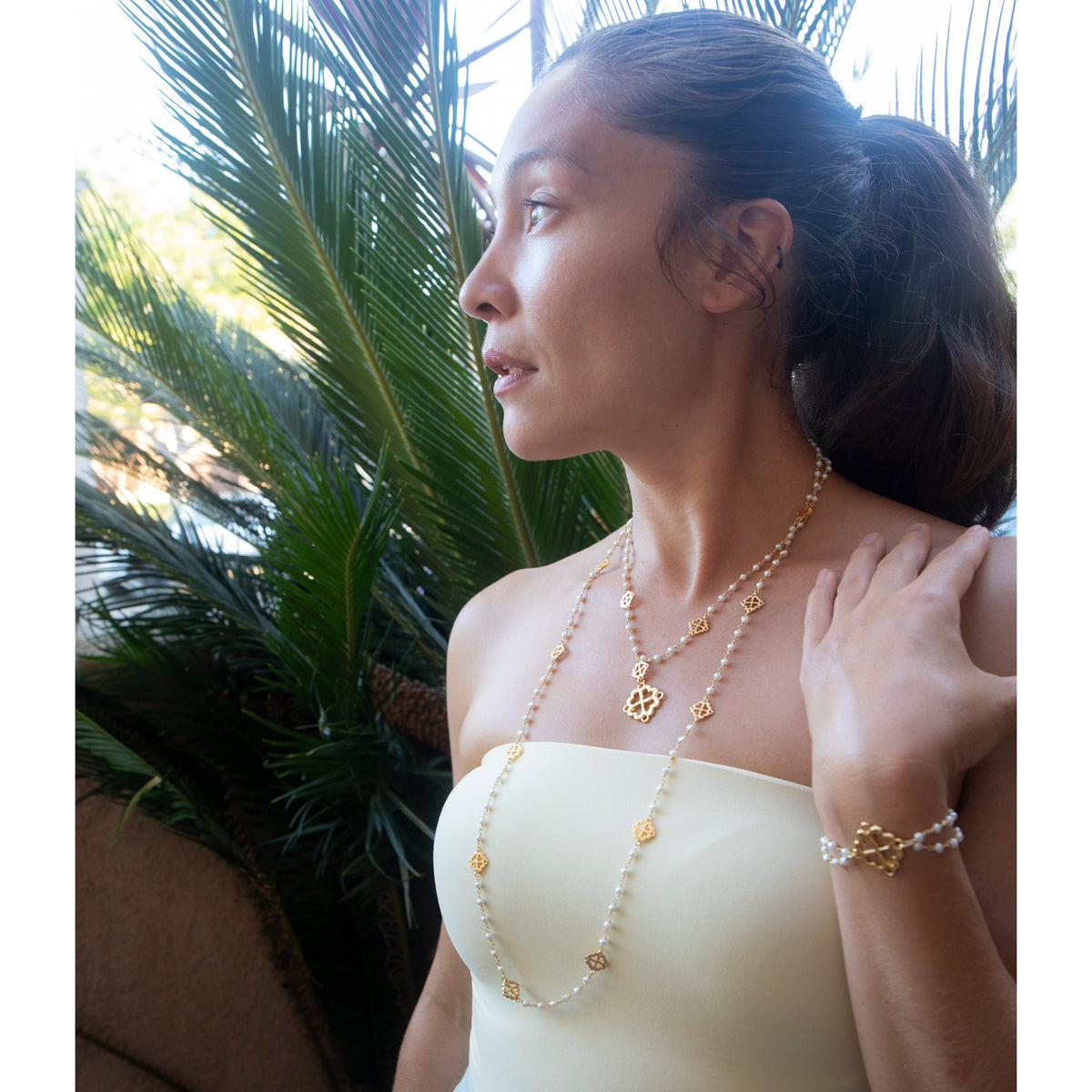 Woman wearing gold jewelry with a tropical background