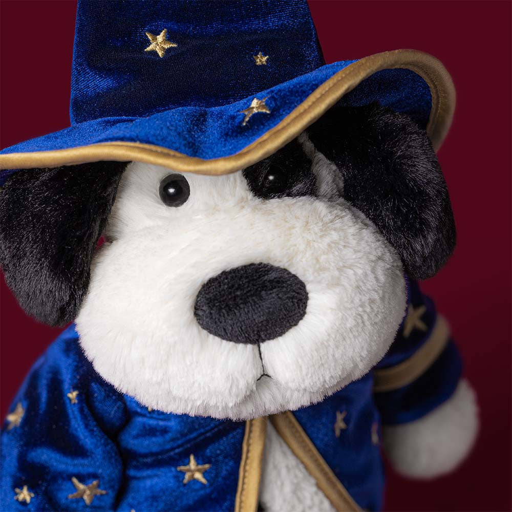 A plush dog toy dressed as a wizard, featuring a navy blue velvet robe and pointed hat with gold star patterns and trim, set against a plain white background.