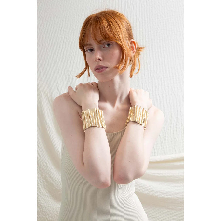 A wide, textured gold cuff bracelet displayed on a white ceramic mannequin neck against a white background.