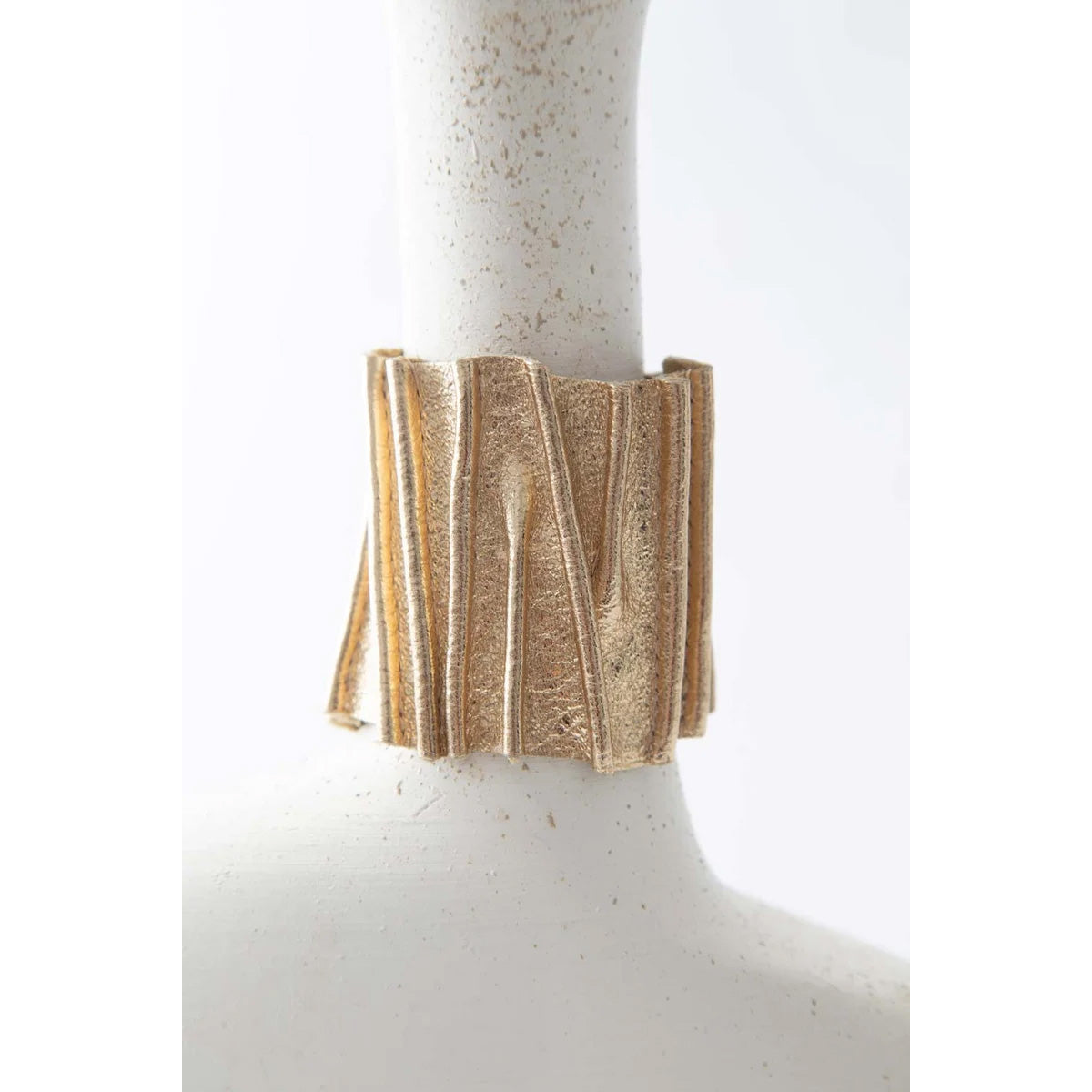 A wide, textured gold cuff bracelet displayed on a white ceramic mannequin neck against a white background.