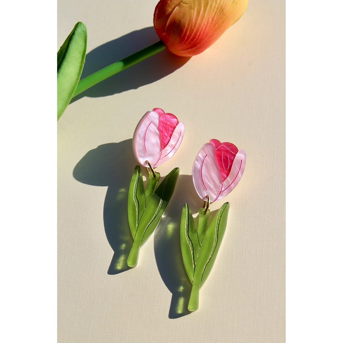Tulip-shaped earrings on a light surface with a tulip in the background