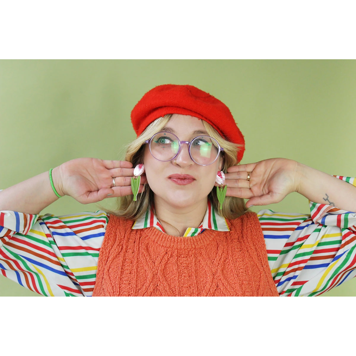 Person wearing a red beret and colorful striped shirt with a green background