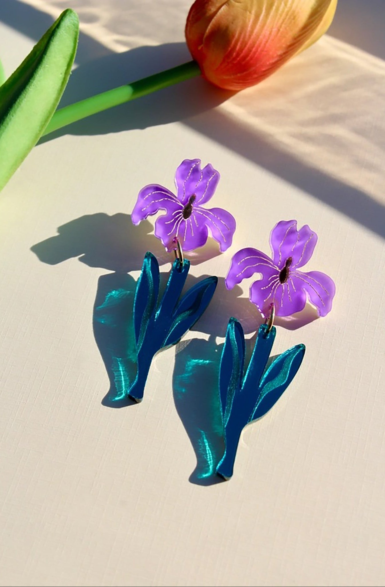 Purple flower-shaped earrings with blue leaves on a light surface.