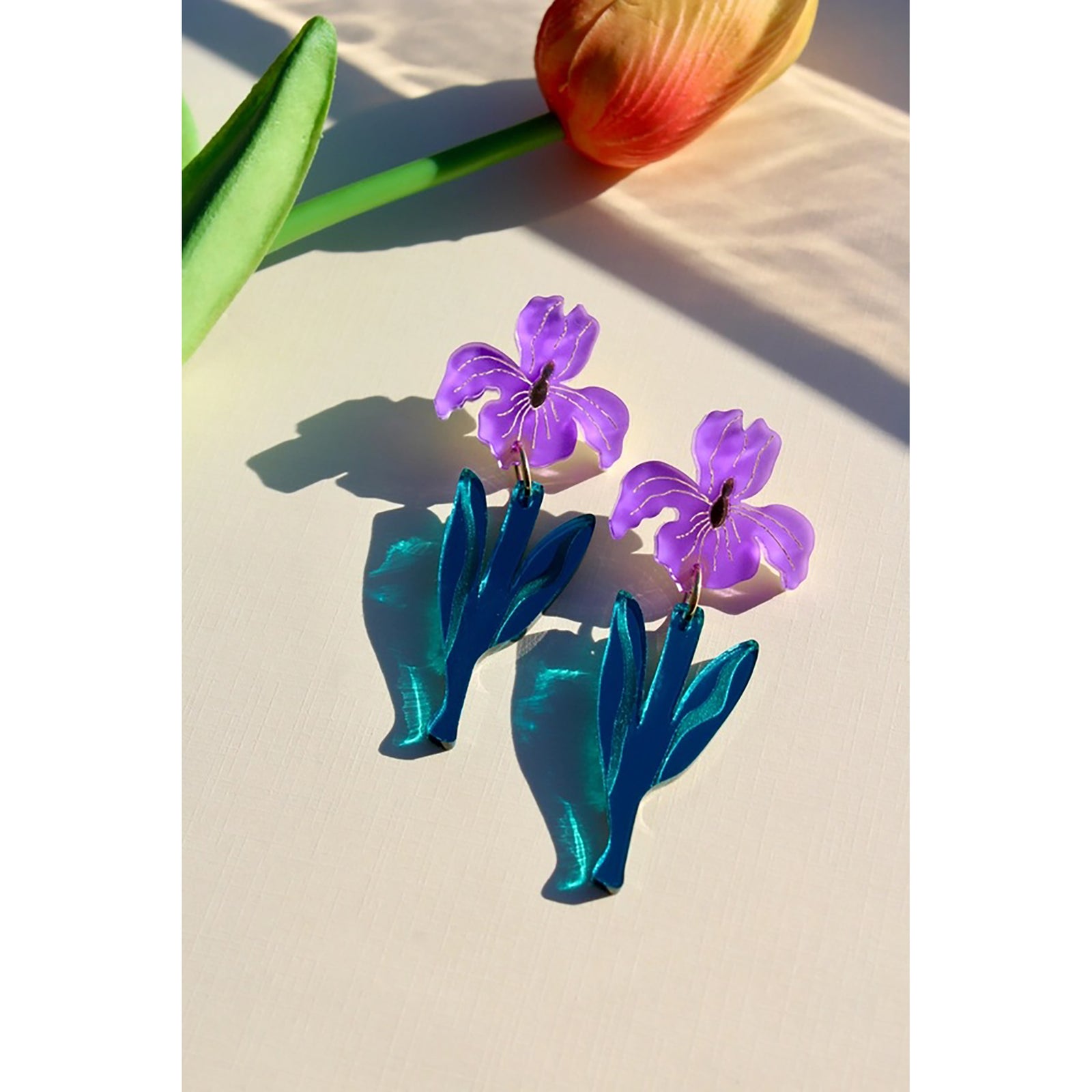 Purple flower-shaped earrings with blue leaves on a light surface.