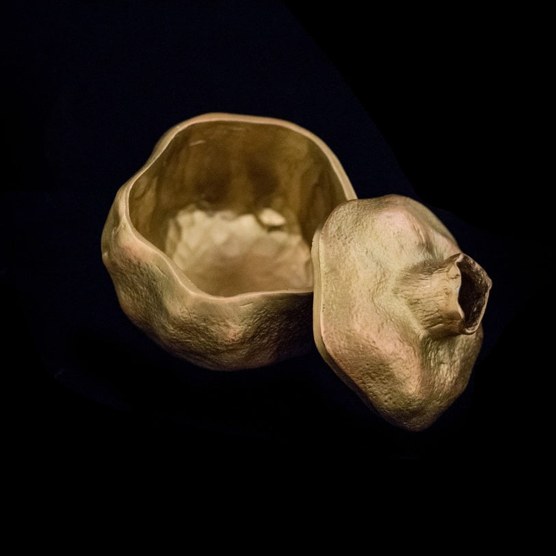 A pewter trinket box with an antique brass finish, designed to resemble an open pomegranate with a removable top, set against a light background.