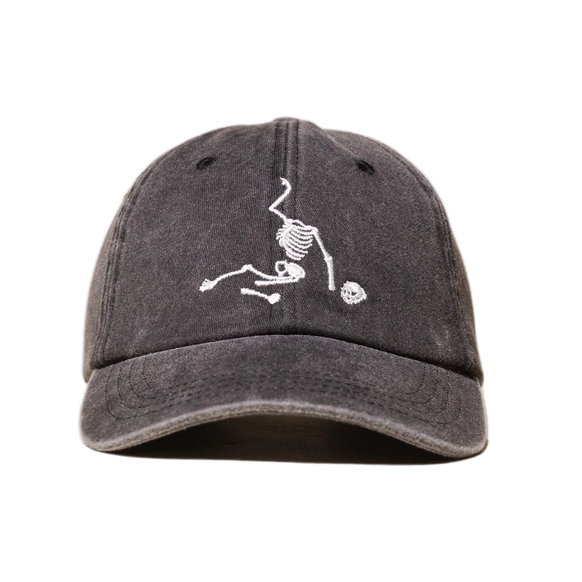 A dark gray washed baseball cap featuring a white embroidered graphic of a skeleton holding a soccer ball on the front, set against a plain white background.
