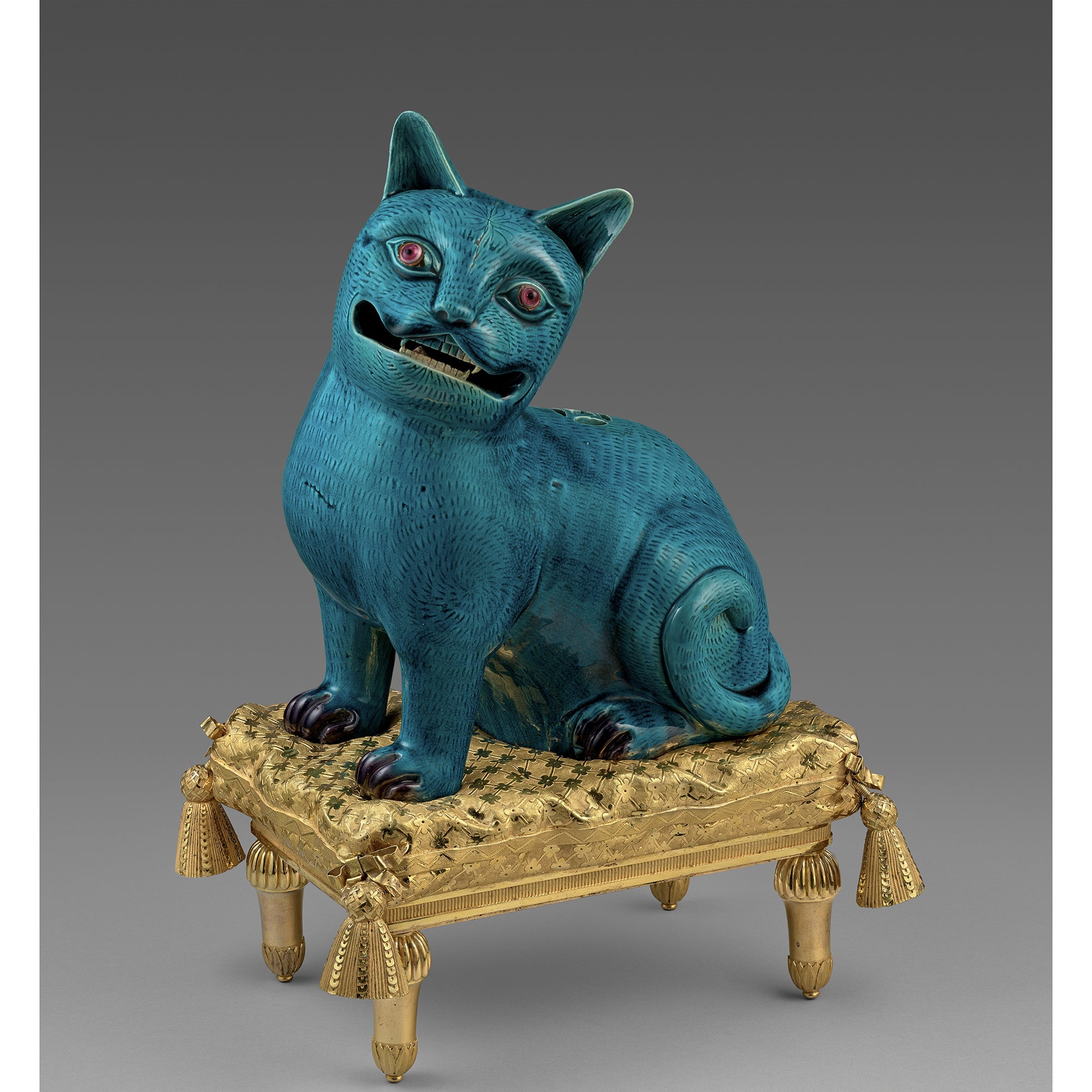 Blue cat figurine on a gold stand against a white background