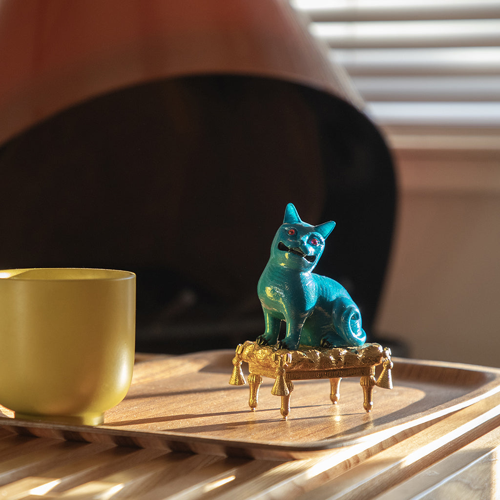 Blue cat figurine on a stand next to a gold cup on a wooden surface.