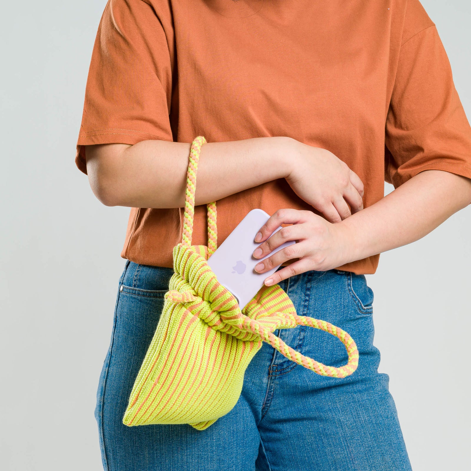 A striped green and peach mini tote bag with hand-knotted macrame handles and a drawstring closure.