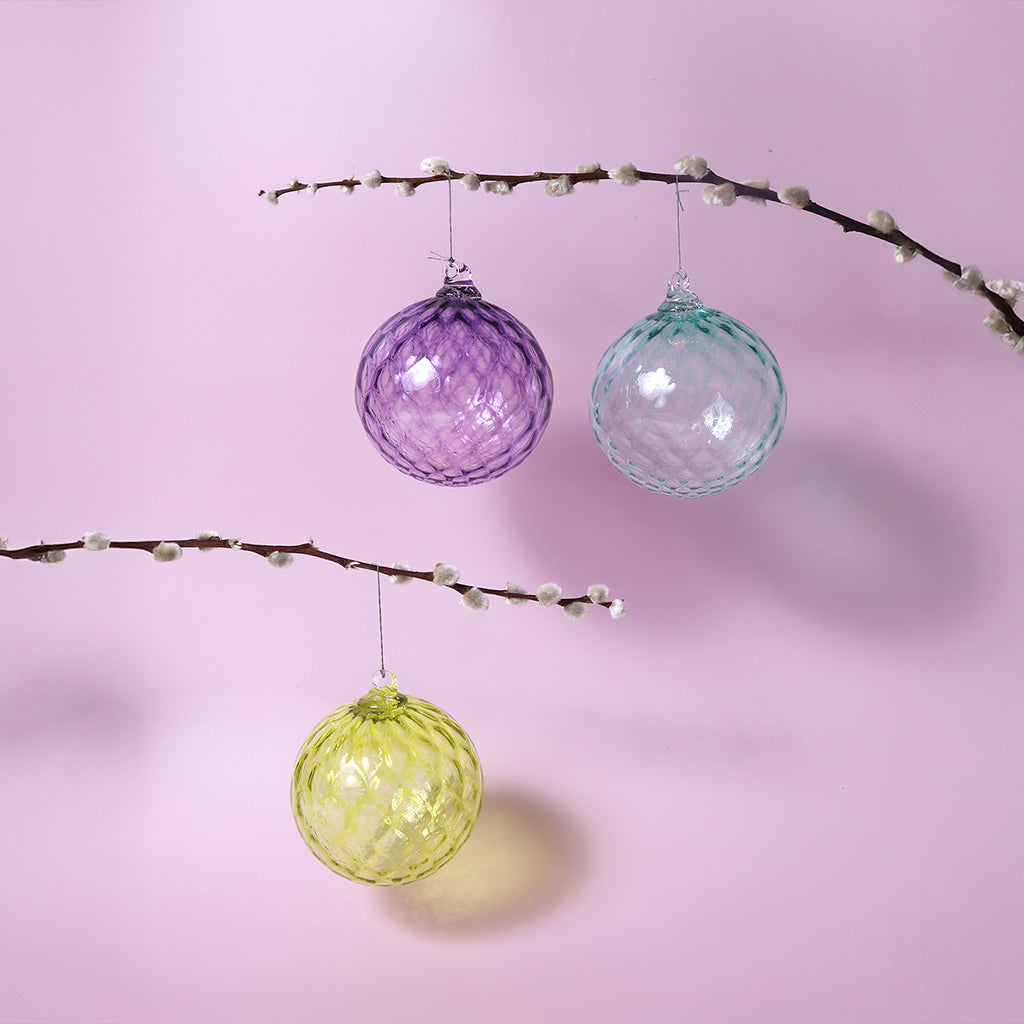 Three colorful glass ornaments hanging from branches against a pink background