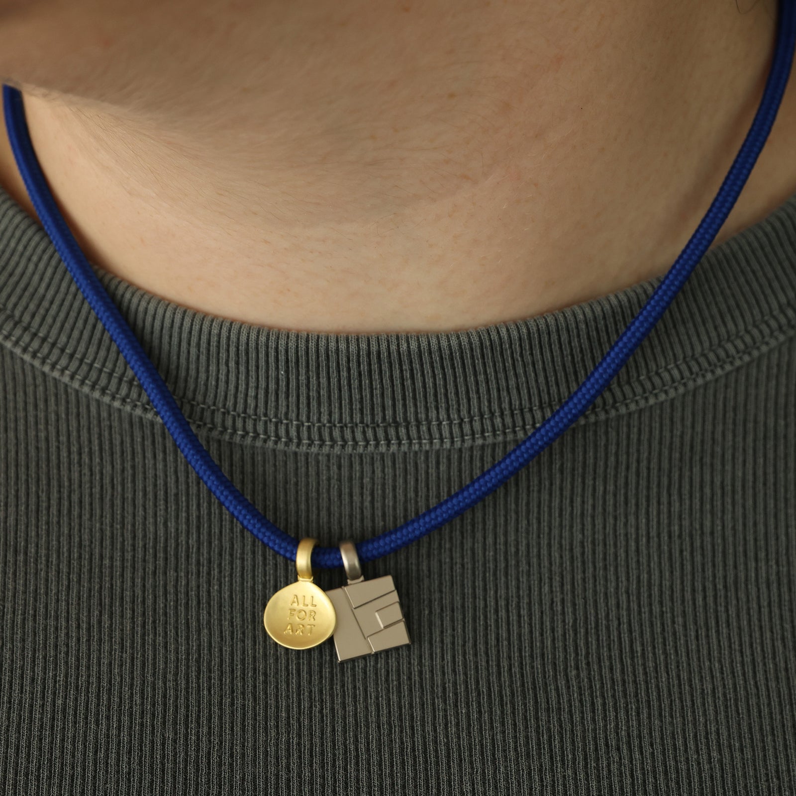 A gold teardrop-shaped pendant with a loop at the top and the words 'ALL FOR ART' engraved on the front, shown against a plain white background.