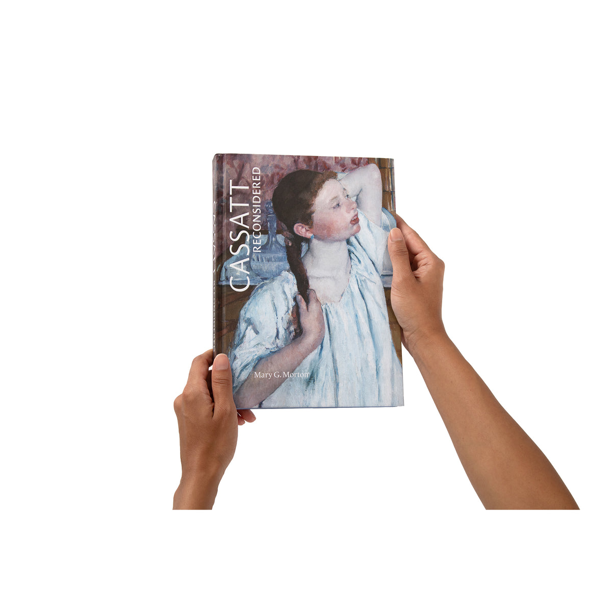 A person holds a hardcover book against a plain white background. The book cover features a painted portrait of a woman in a light blue dress, and the person's hands and forearms are visible holding the book.