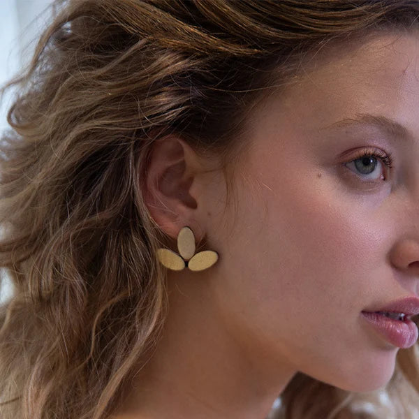 A close-up side profile of a woman with wavy light brown hair wearing a small natural wood flower-shaped stud earring.