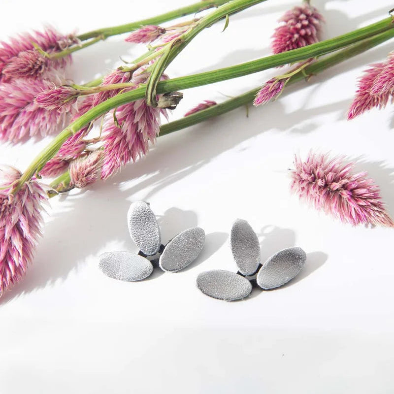 Three pairs of textured gold oval stud earrings arranged on a white surface with decorative pink dried flowers in the background.