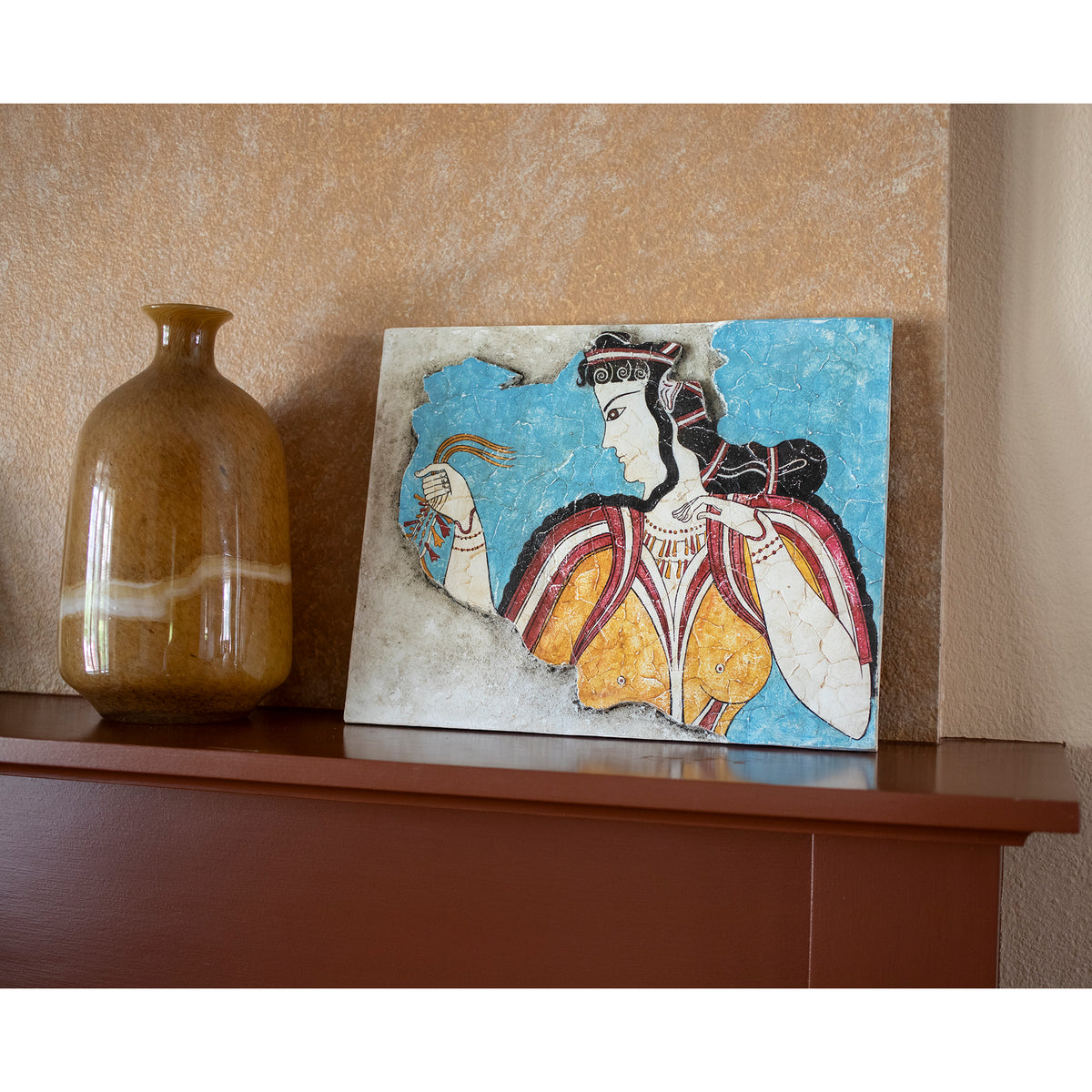 Decorative tile with a woman&#39;s portrait and a brown vase on a shelf against a beige wall.