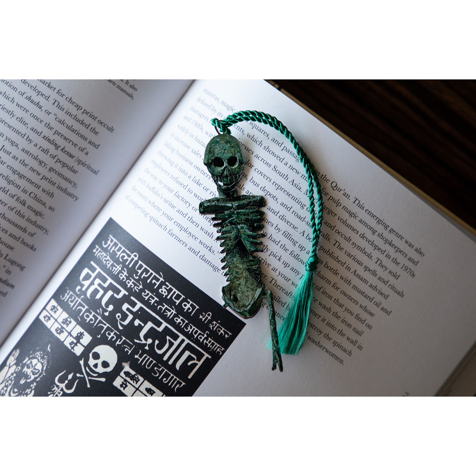 A metal bookmark in the shape of a Roman miniature bronze skeleton with a green tassel.