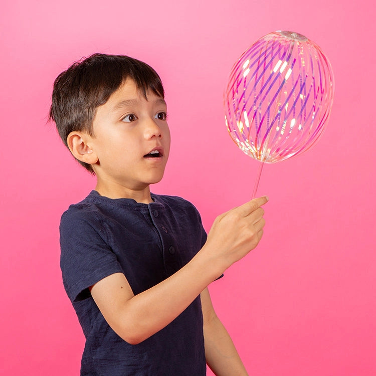 Child holding a colorful balloon against a pink background