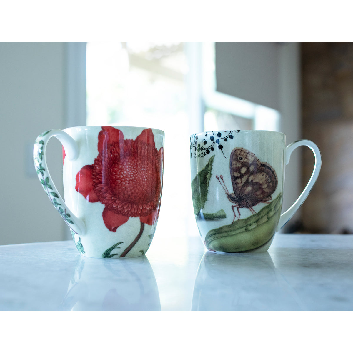 Two mugs with floral and butterfly designs on a marble surface.