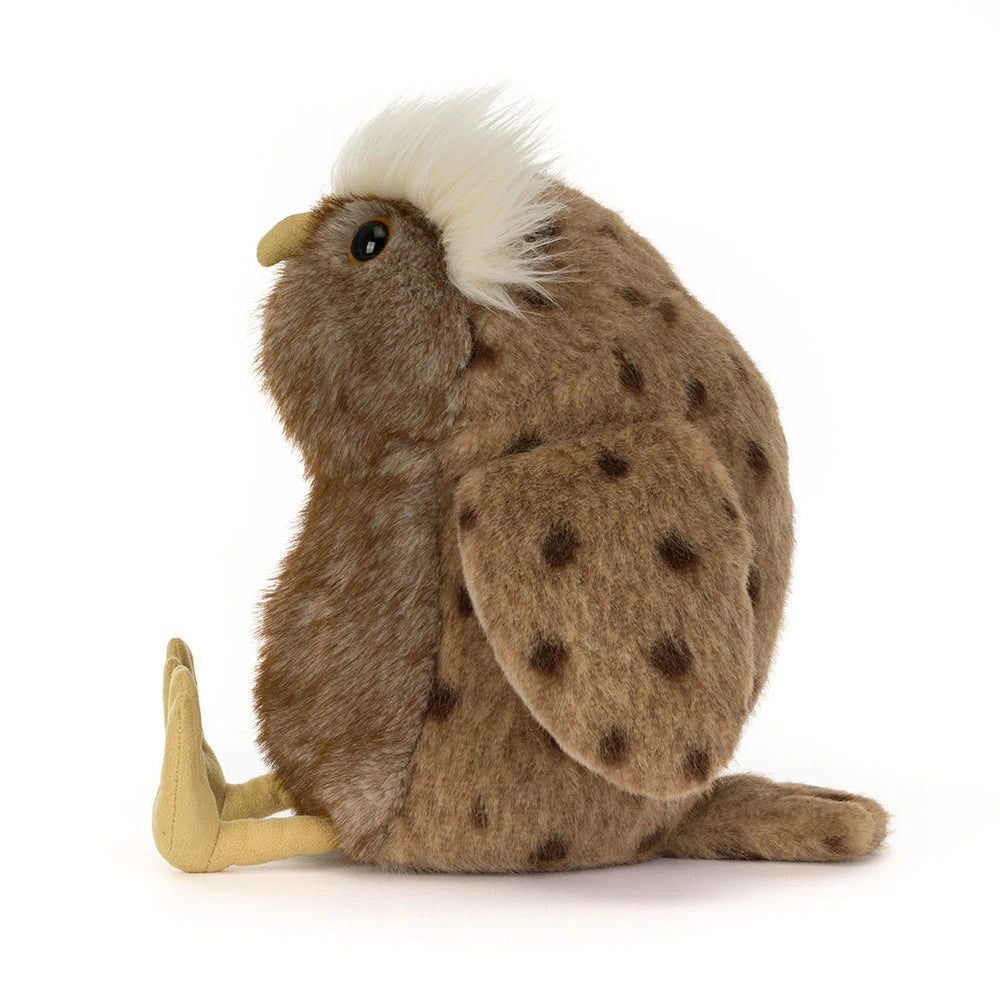 A plush stuffed animal shaped like a brown spotted bird, shown from the side on a clean white background. The bird has a fluffy white crest on its head, a yellow beak, tan legs, and dark brown spots across its brown fur.