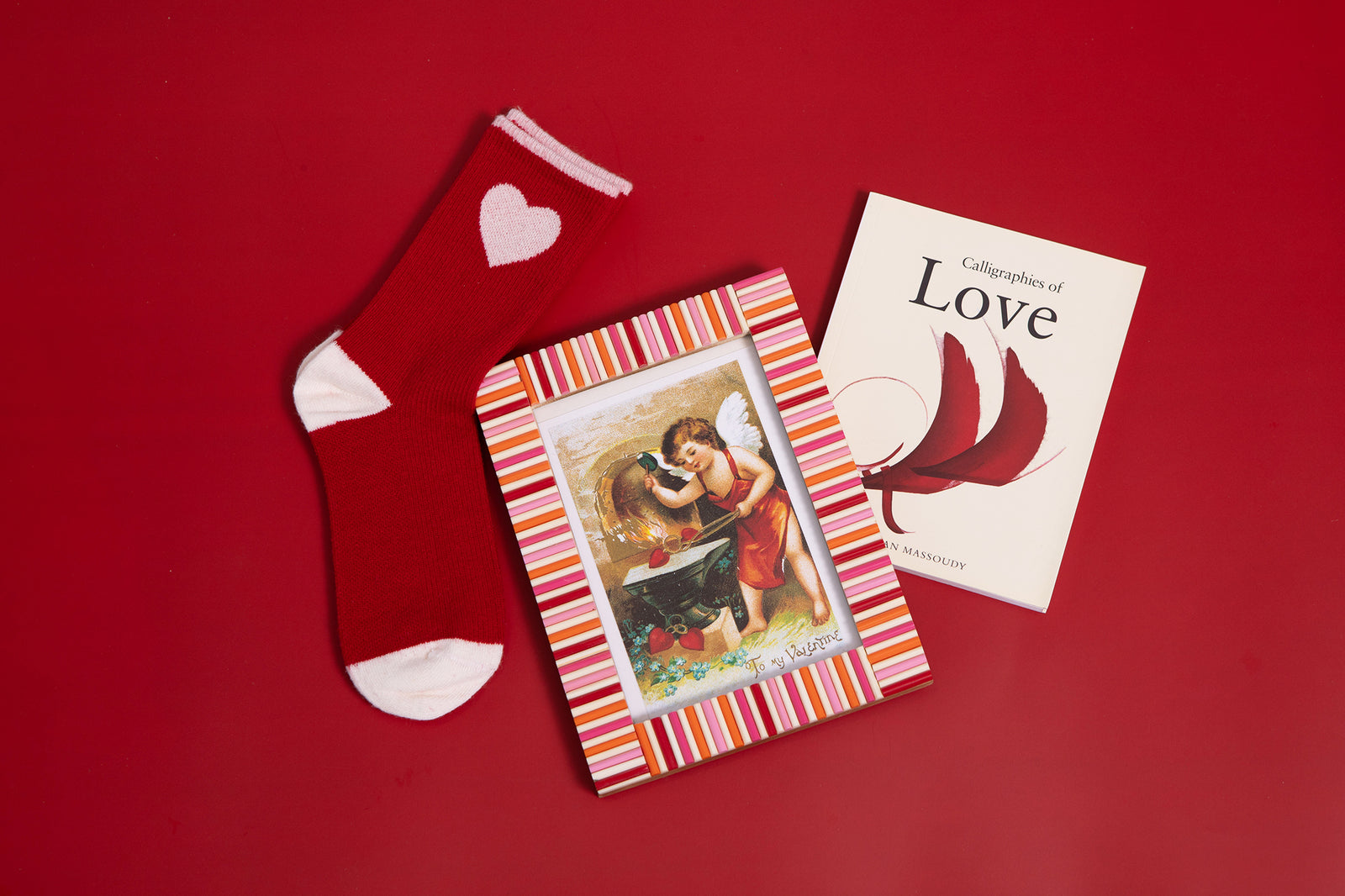 Red sock with heart design, card with striped border, and book titled 'Calligraphies of Love' on a red background