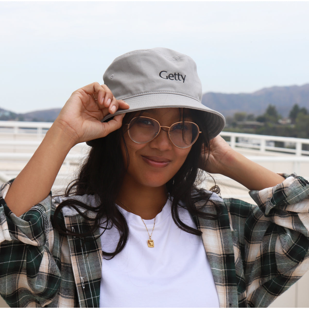 Model wearing Gray Getty Embroidered Bucket Hat in front of mountains