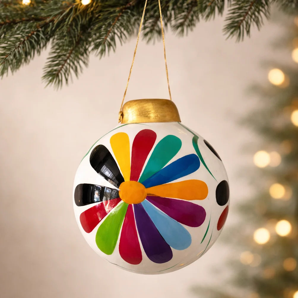 Colorful floral-patterned Christmas ornament hanging on a tree with blurred lights in the background.