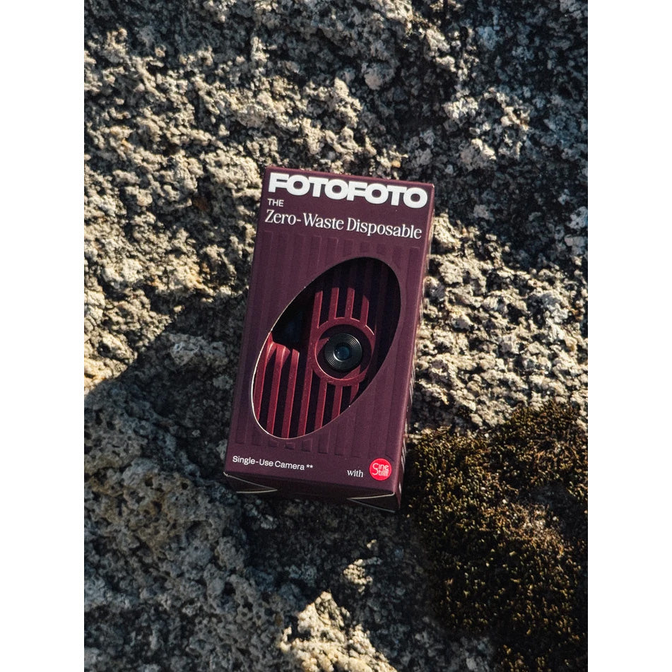 A boxed disposable camera product labeled POTOFOTO Zero-Waste Disposable, shown standing on rough rock outdoors.