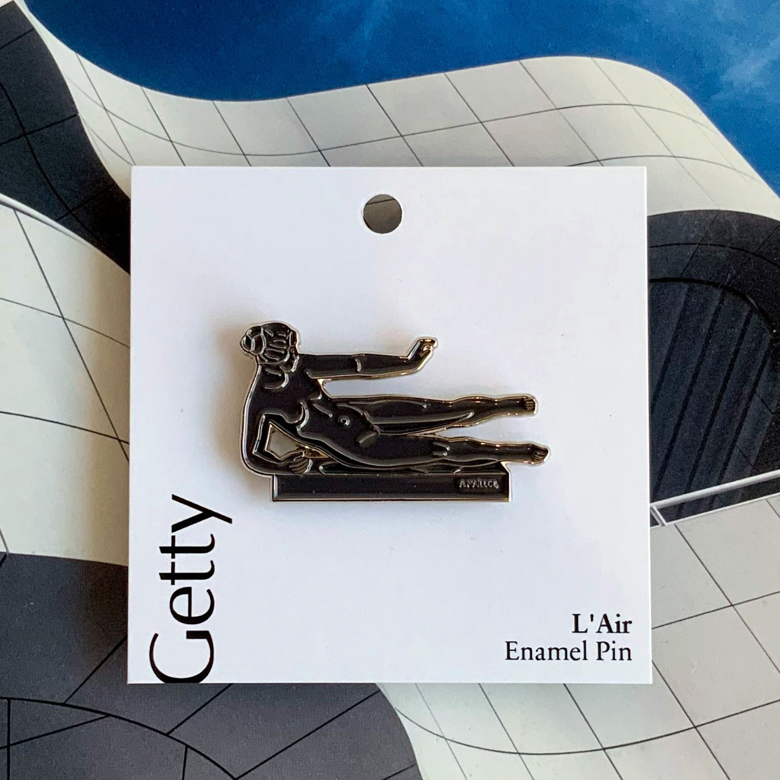 An enamel pin featuring a sculptural representation of a figure, reminiscent of a classical statue, in black and white.