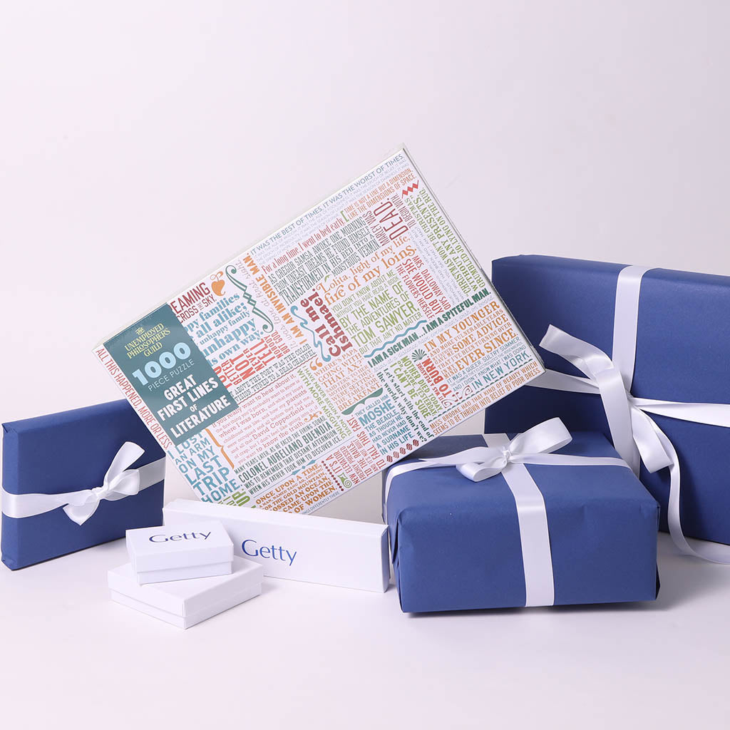 A boxed set of books presented with blue gift boxes and white ribbons on a clean white background. One box is open to reveal a book titled '1000 Great First Books in Literature,' and smaller white boxes with the Getty logo are arranged in front.