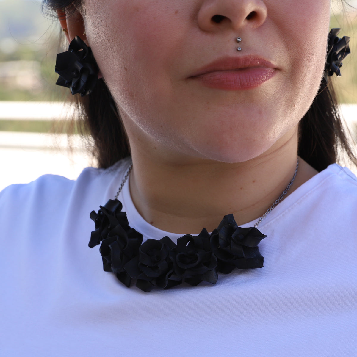 Person wearing a black floral necklace and earrings with a blurred outdoor background