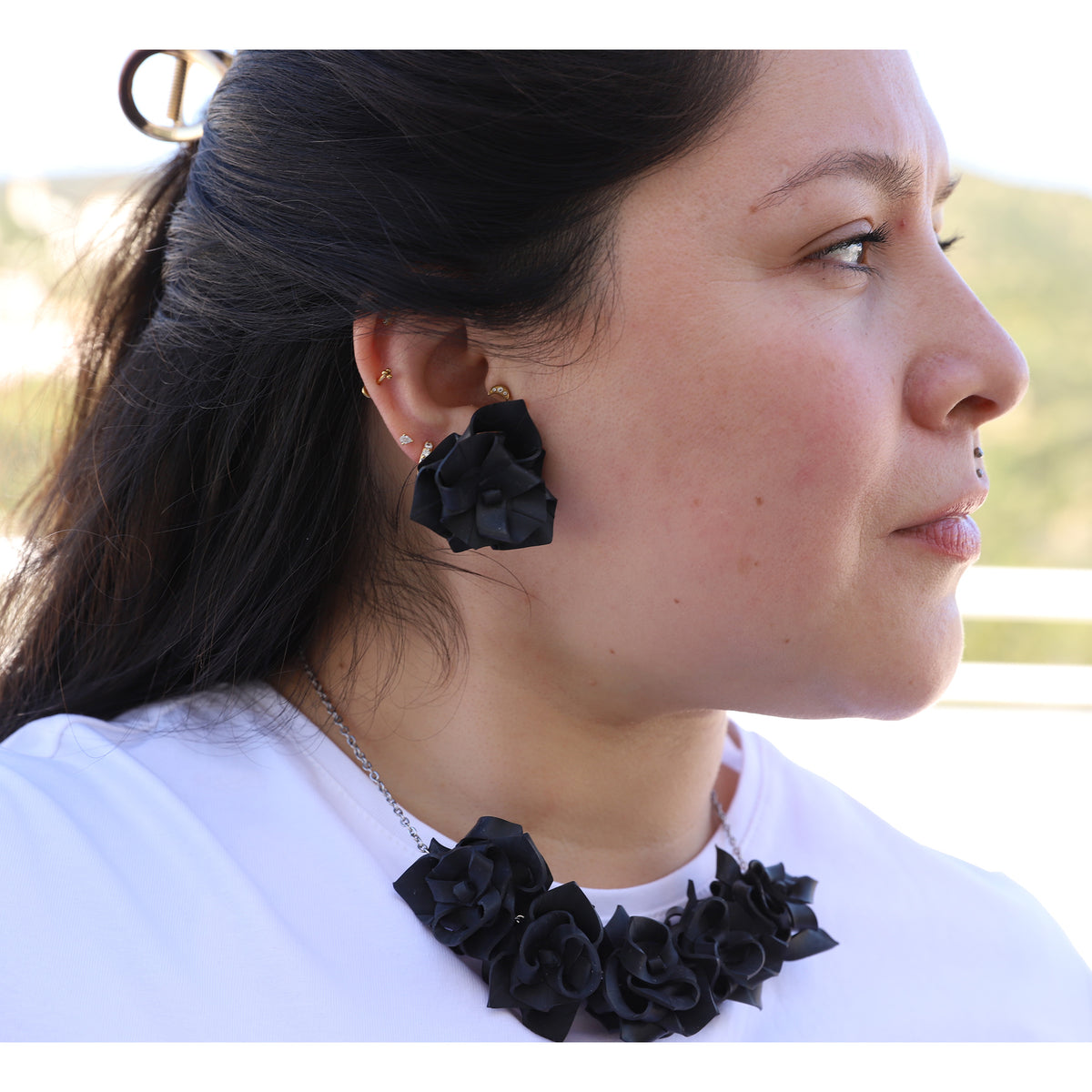 Woman wearing black floral earrings and a matching necklace outdoors.