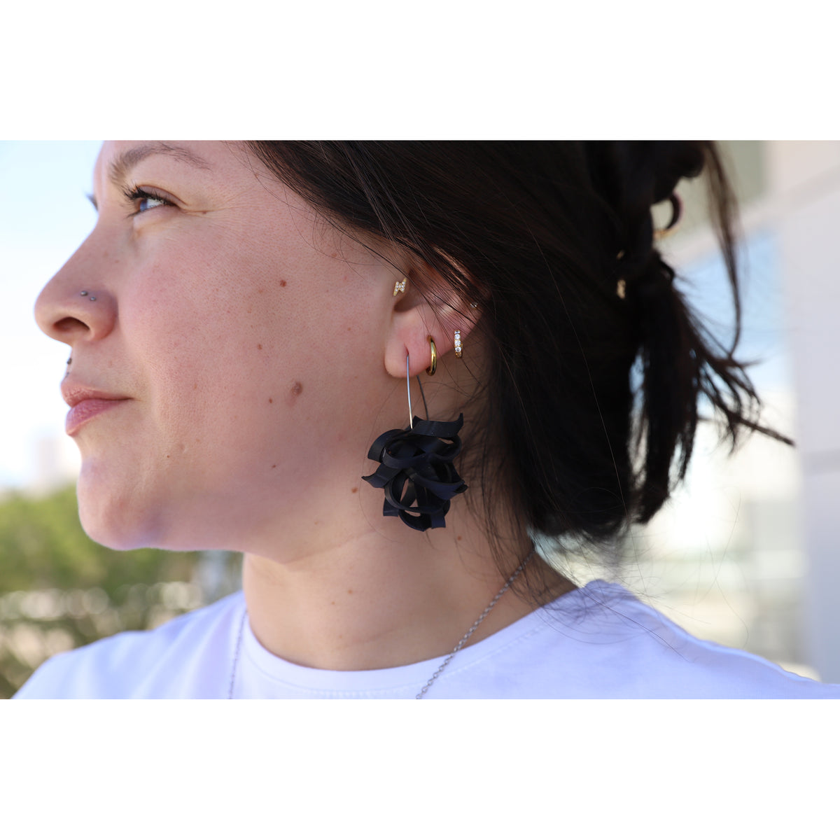 Close-up of a person wearing black floral earrings with a blurred outdoor background