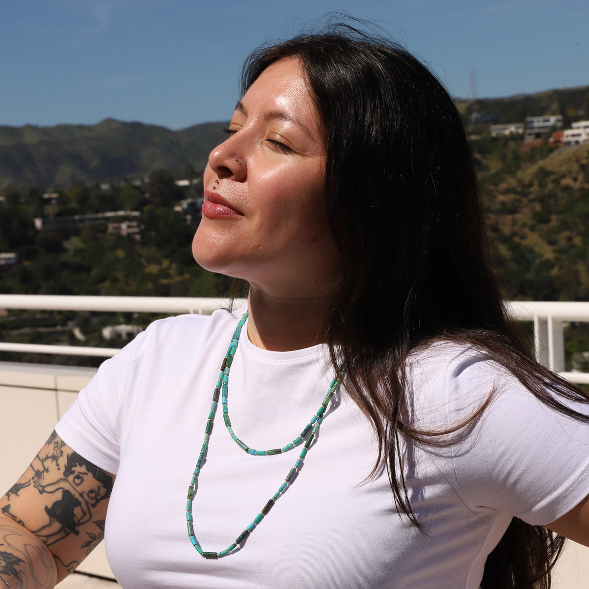 Woman wearing a white shirt and green necklace with a scenic background